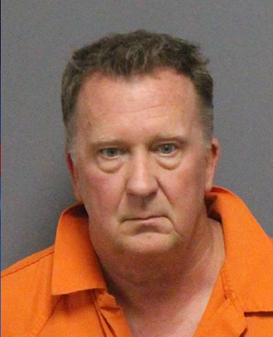 White man in his fifties, bluish/gray eyes. brown hair, huge bags under eyes, attached earlobes, puffy cheeks with deep lines from nose to mouth and mouth to chin. orange jumpsuit. 